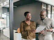 Two office workers examine a handheld tablet